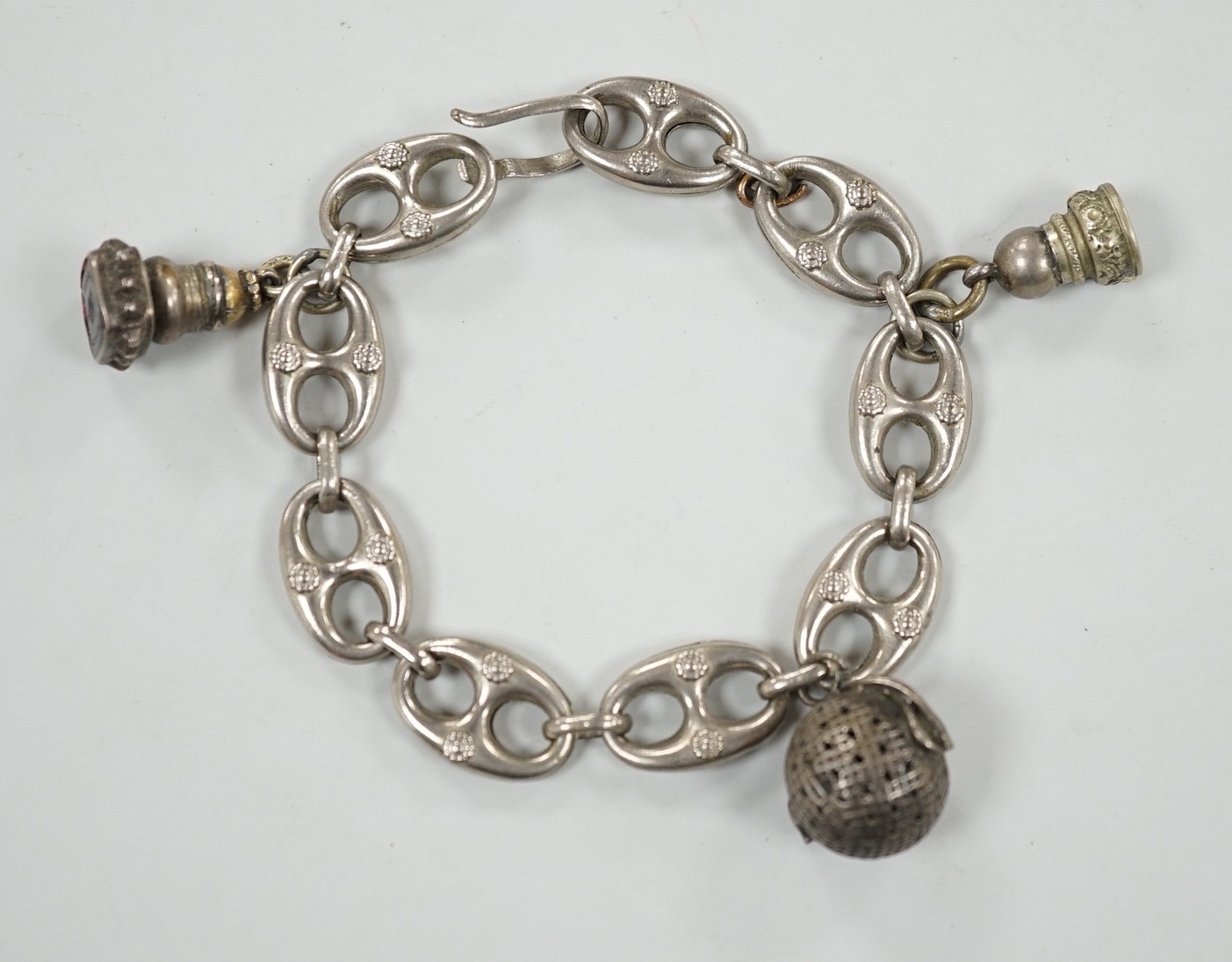 A white metal oval link bracelet, hung with three charms, including two fob seals, 21cm.